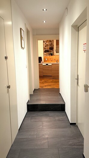 A hallway with a wooden floor leading to a kitchen area with a stone wall backsplash.