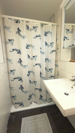 Une salle de bain avec un rideau de douche orné d’un motif d’oiseaux, un lavabo blanc et un miroir au-dessus du lavabo.