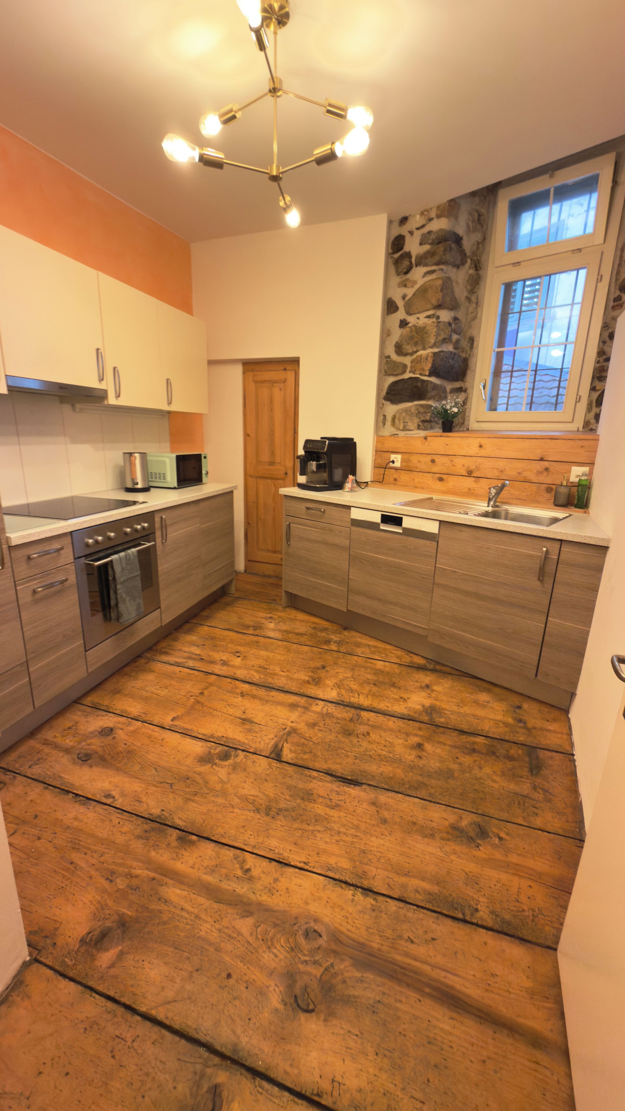 A kitchen with wooden flooring, a stone wall, and a window with a view.
