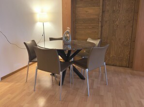 Une table ronde avec un plateau en verre, entourée de quatre chaises, une lampe et une porte en bois en arrière-plan.