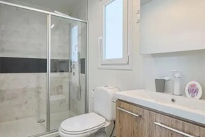 Ein Badezimmer mit Duschkabine aus Glas, Toilette und Waschtisch mit Spiegel.