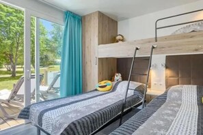 Ein Zimmer mit einem Etagenbett, einem Fenster mit Blick auf Grünflächen und einem Tisch mit Stühlen draußen.