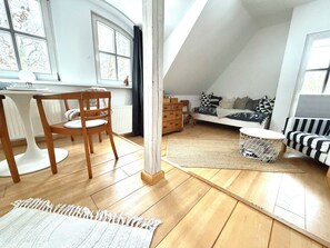 A cozy loft bedroom with a sloped ceiling, a wooden dining table, a sofa, and a patterned rug. - Vacation Rental in the Countryside Near Bremen – 90 square meters for up to 5 people (Ritterhude)