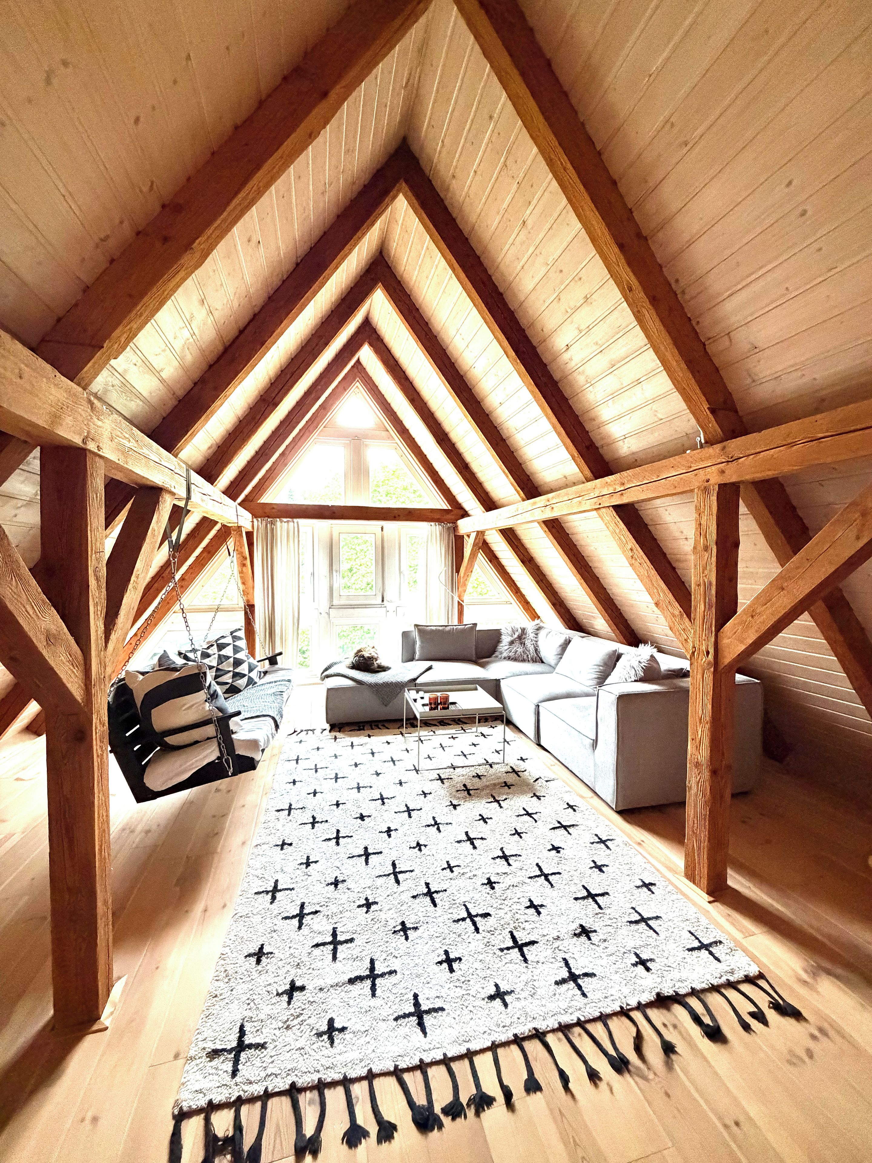An attic room with a sloped wooden ceiling, a sofa, a coffee table, and a patterned rug.