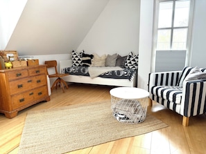 A loft-style bedroom with a sloped ceiling, a bed with patterned bedding, a striped armchair, a wooden dresser, and a round wire basket. - Vacation Rental in the Countryside Near Bremen – 90 square meters for up to 5 people (Ritterhude)