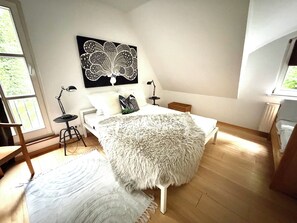 A bedroom with a bed, a fluffy rug, a desk, a chair, a standing lamp, and a wall-mounted artwork. - Vacation Rental in the Countryside Near Bremen – 90 square meters for up to 5 people (Ritterhude)