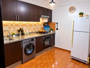 Eine kompakte Küche mit dunklen Holzschränken, einem eingebauten Geschirrspüler, einem Herd und einem Samsung-Kühlschrank.