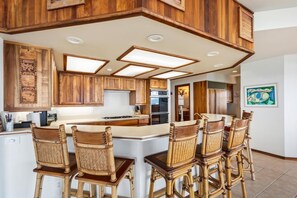 A kitchen with wooden cabinets, a central island with bar stools, and recessed lighting. - Big Island Ali'i Point 11 3 Bedroom Home (Kailua-Kona)