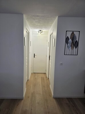 A hallway with a white door at the end, a ceiling light, and a wall-mounted art piece.