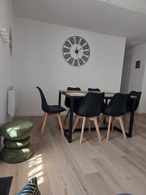 Een eetgedeelte met een houten tafel, zwarte stoelen en een klok aan de muur.