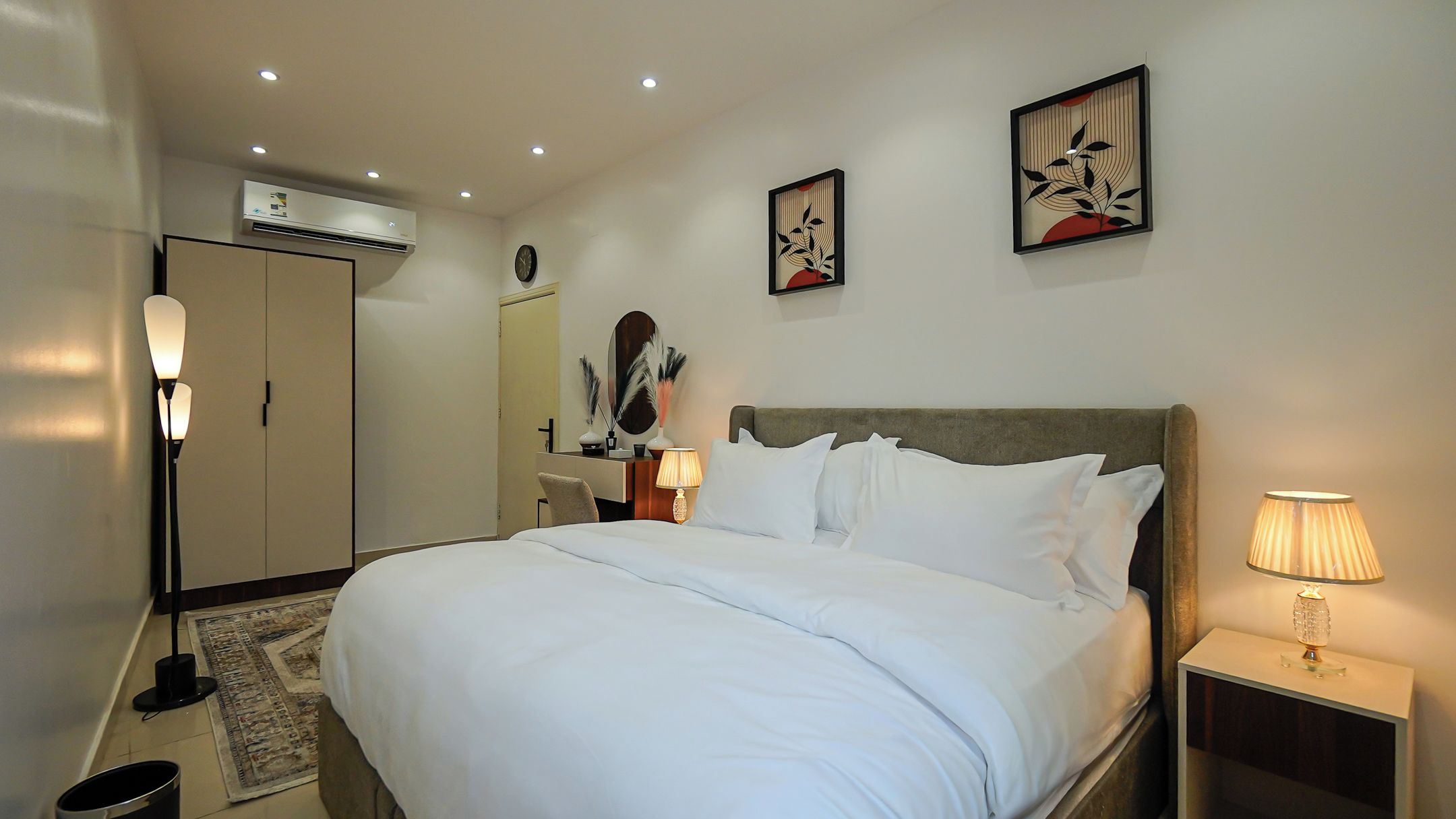 Una habitación de hotel con cama, lámpara de noche, decoración en la pared y un equipo de aire acondicionado.