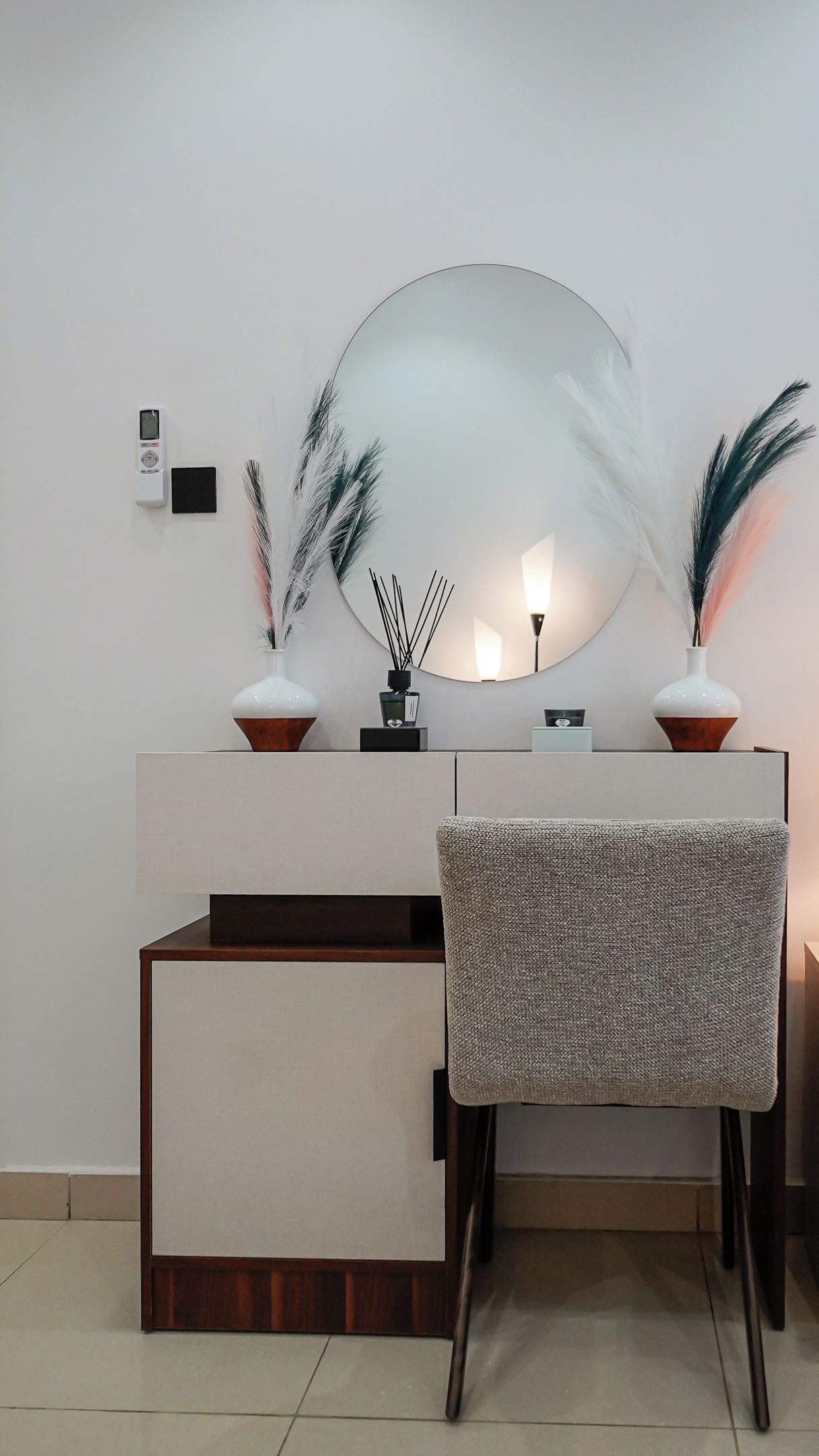Un baño moderno con un espejo grande, dos jarrones con plumas decorativas, un pequeño dispositivo digital y una silla con textura.