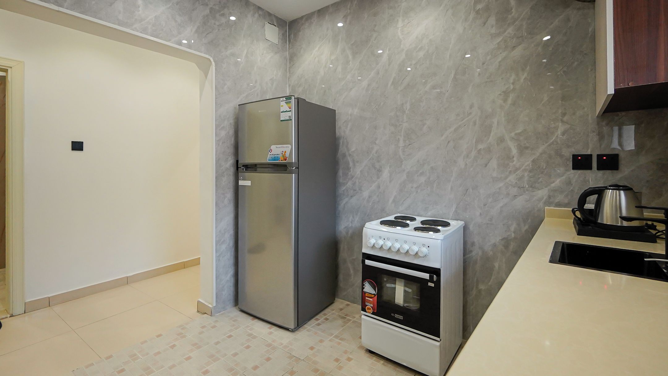 Una cocina compacta con refrigerador, estufa y hervidor sobre la encimera.