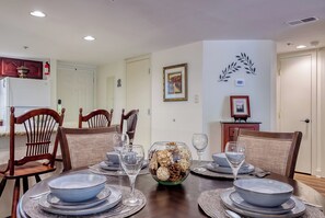 A dining area with a table set for four, chairs, a decorative centerpiece, and a wall-mounted thermostat. - Creekside Balcony~ Mountain View~ Downtown Gatlinburg~Pool (Gatlinburg)