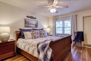 A bedroom with a wooden bed, two bedside tables with lamps, a ceiling fan, a window with curtains, and a door. - Creekside Balcony~ Mountain View~ Downtown Gatlinburg~Pool (Gatlinburg)