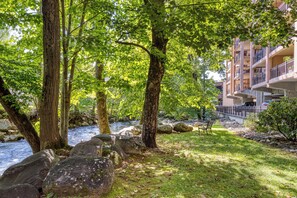 A riverside view with trees, a grassy area, and a building with balconies. - Creekside Balcony~ Mountain View~ Downtown Gatlinburg~Pool (Gatlinburg)