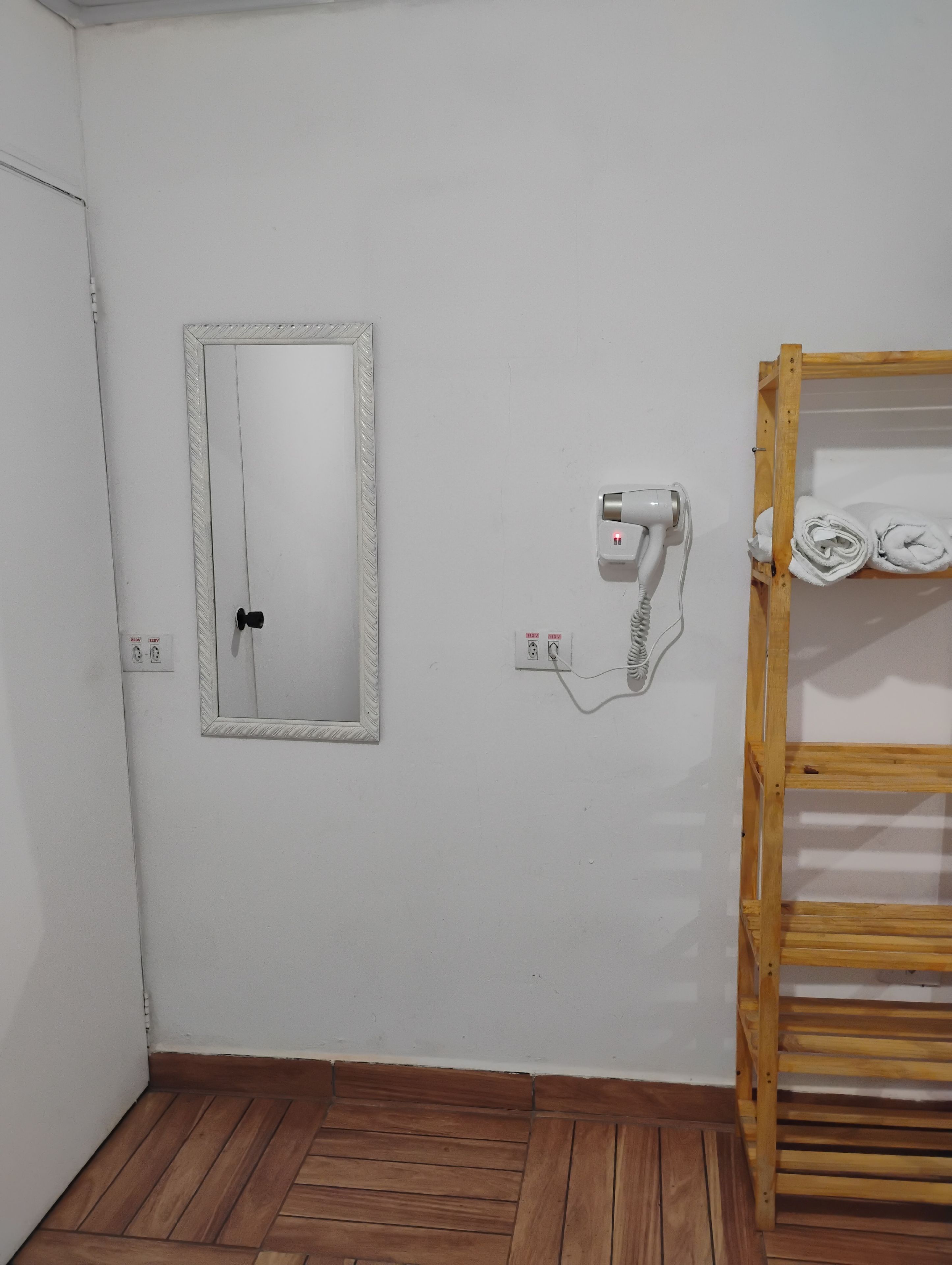 Un baño con suelo de madera, un espejo, un secador de pelo y un perchero para toallas.