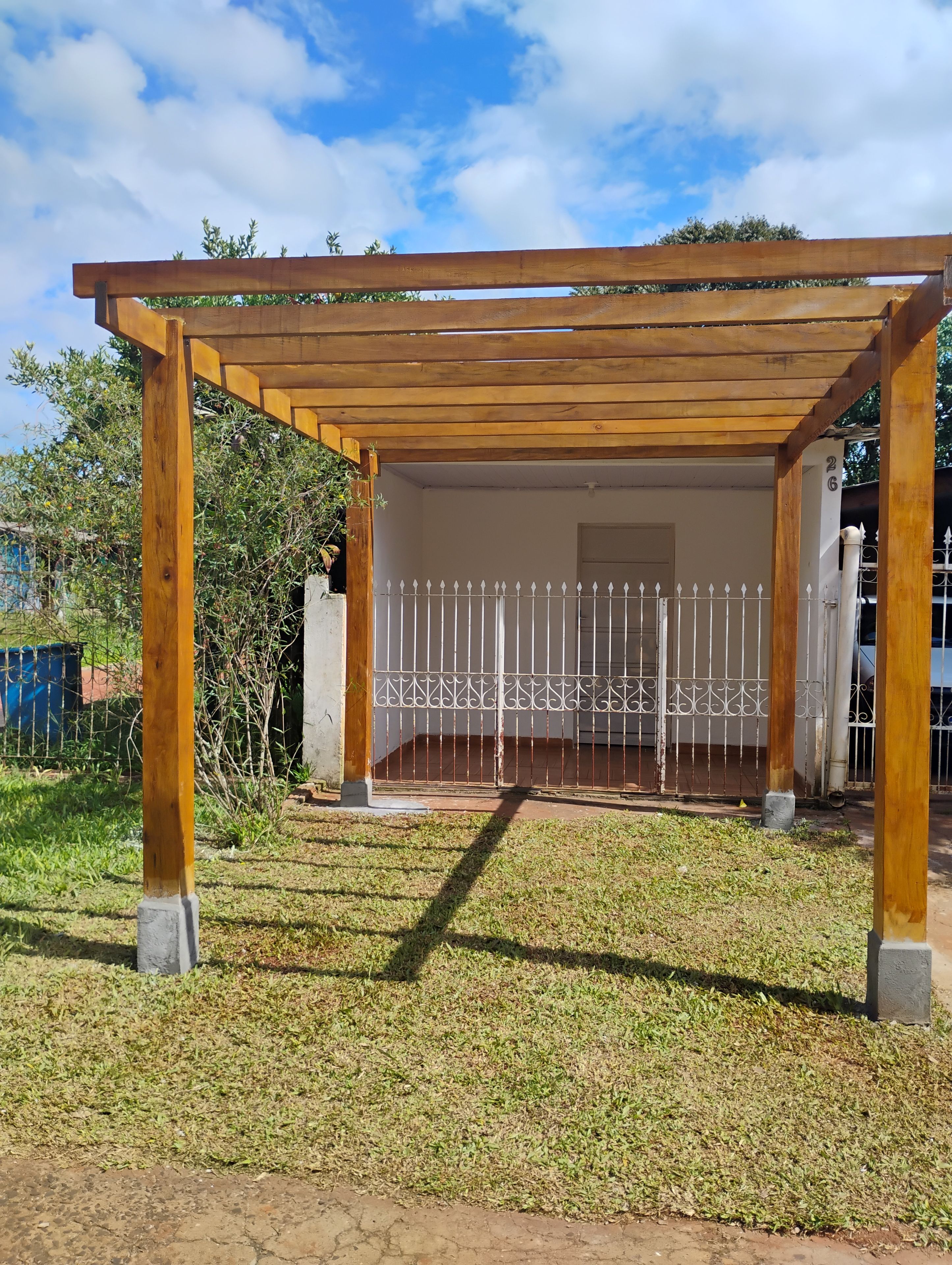 Una estructura de pérgola de madera con un portón metálico blanco al fondo.