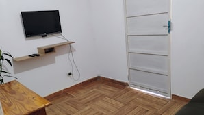 Huoneessa on seinälle asennettu televisio, puulattia, sohva ja ovi, jossa on kahva.