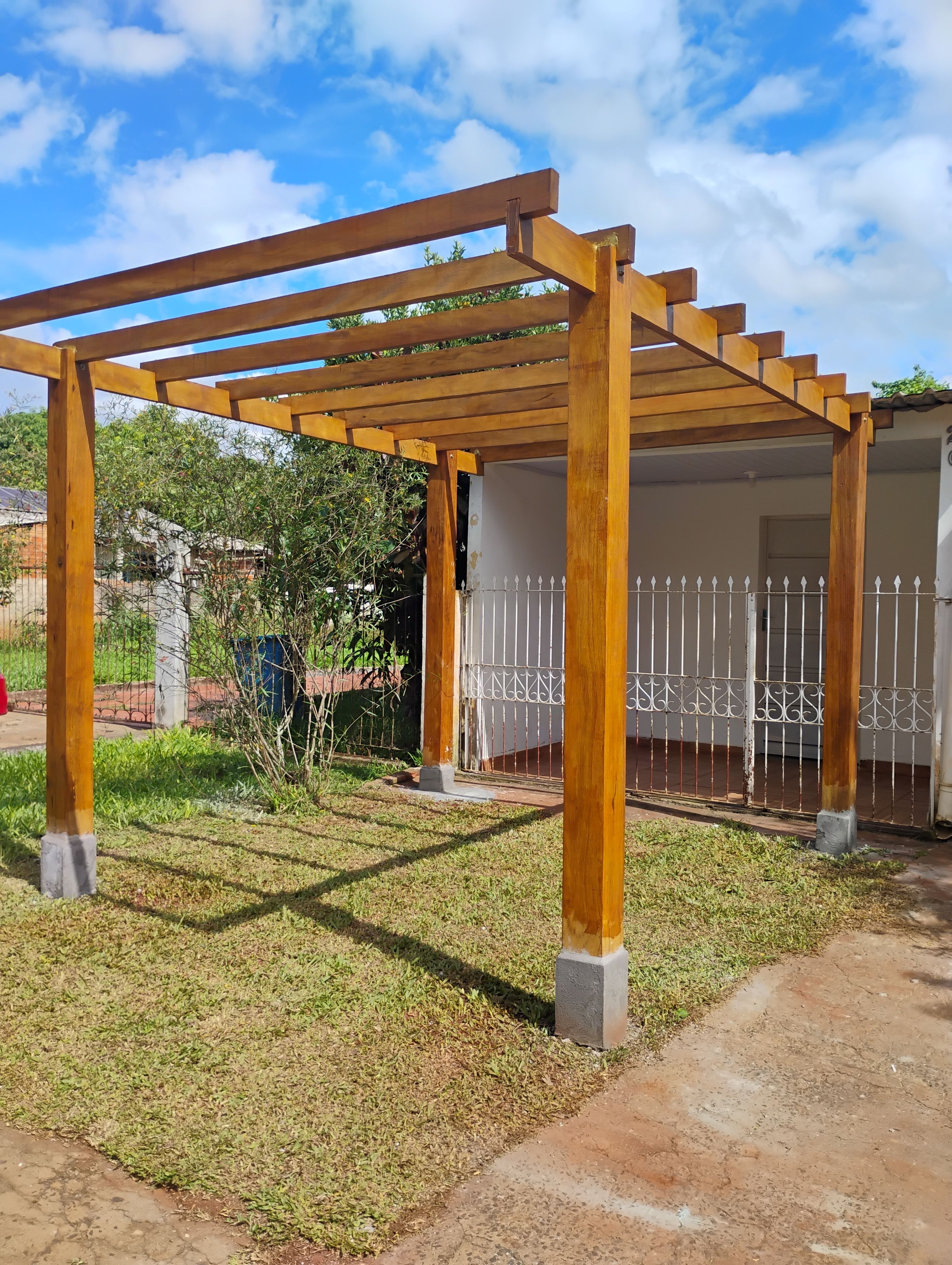 Una struttura in legno a pergola con un recinto bianco sullo sfondo.