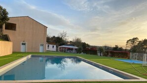 Una piscina rectangular con zonas verdes alrededor y un edificio al fondo.