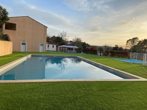 Une piscine rectangulaire entourée d’une pelouse, avec un bâtiment visible à l’arrière-plan.