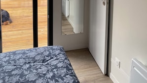 Un dormitorio con cama, una puerta y vistas a una terraza de madera.