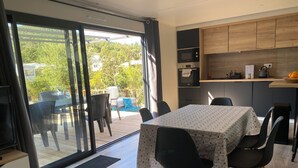 Una cocina moderna con comedor, que incluye una mesa con sillas, horno empotrado y un estante de madera sobre la encimera.