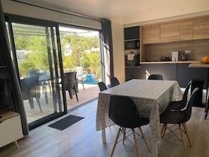 Une cuisine moderne avec un coin repas, comprenant une table avec des chaises, un four encastré et une étagère en bois au-dessus du plan de travail.
