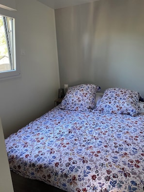 A single bed with floral bedding in a room with a window and a nightstand.