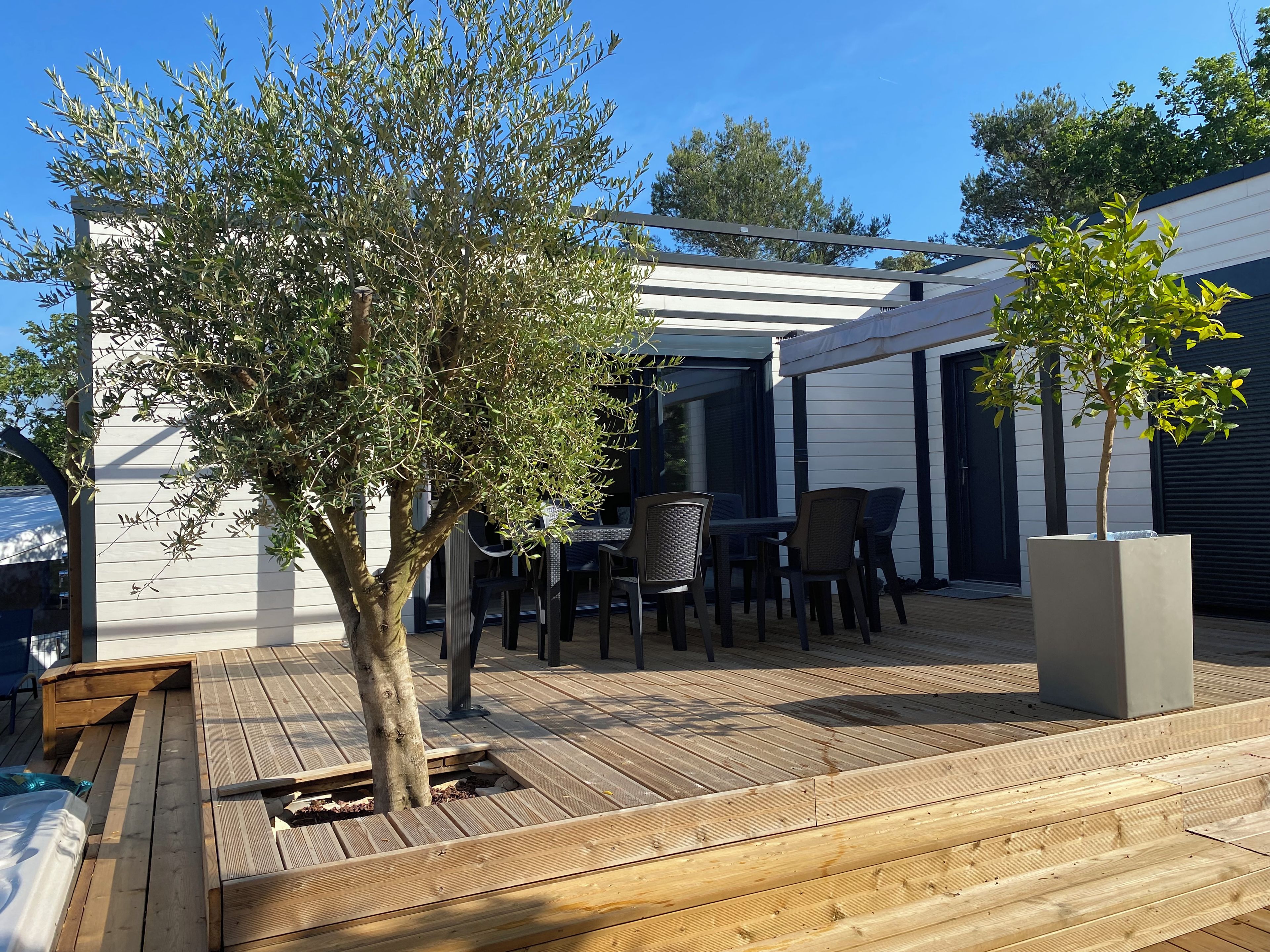 An outdoor patio area with a wooden deck, a table with chairs, and a pergola structure.