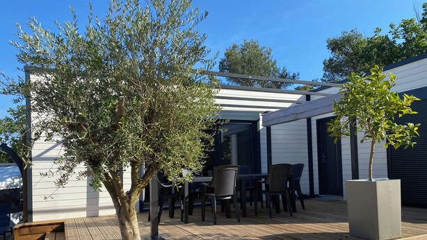 Un patio al aire libre con piso de madera, una mesa y sillas, y una estructura de pérgola.