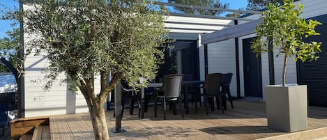 An outdoor patio area with a wooden deck, a table with chairs, and a pergola structure.
