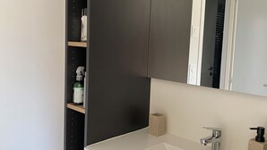 Un baño moderno con un espejo grande, un lavamanos blanco y un mueble oscuro.