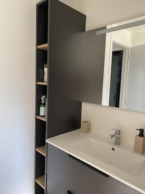 Une salle de bain moderne avec un grand miroir, un lavabo blanc et un meuble sombre.
