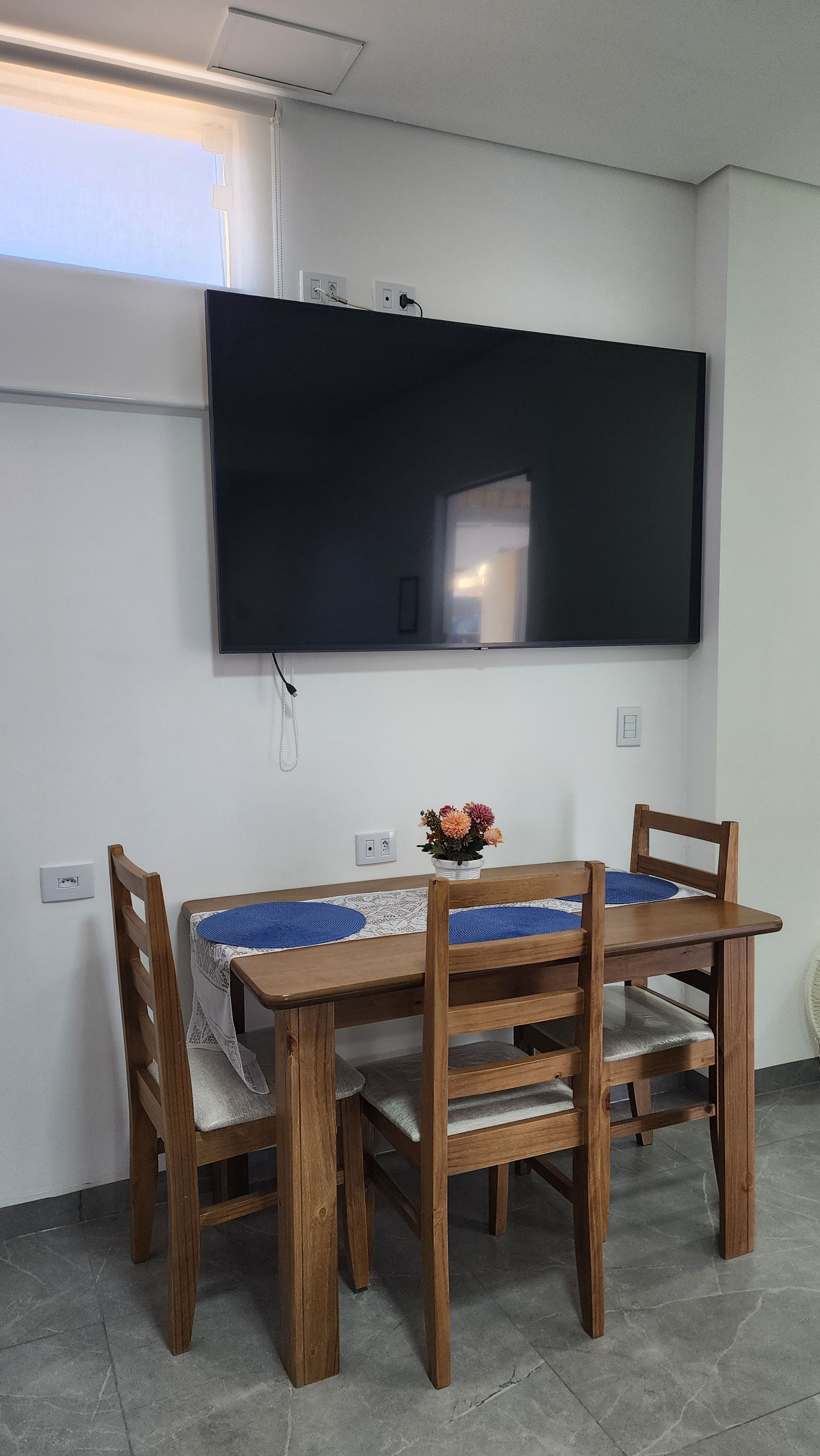 Un comedor con una mesa y sillas, un televisor de pantalla plana en la pared y un florero sobre la mesa.
