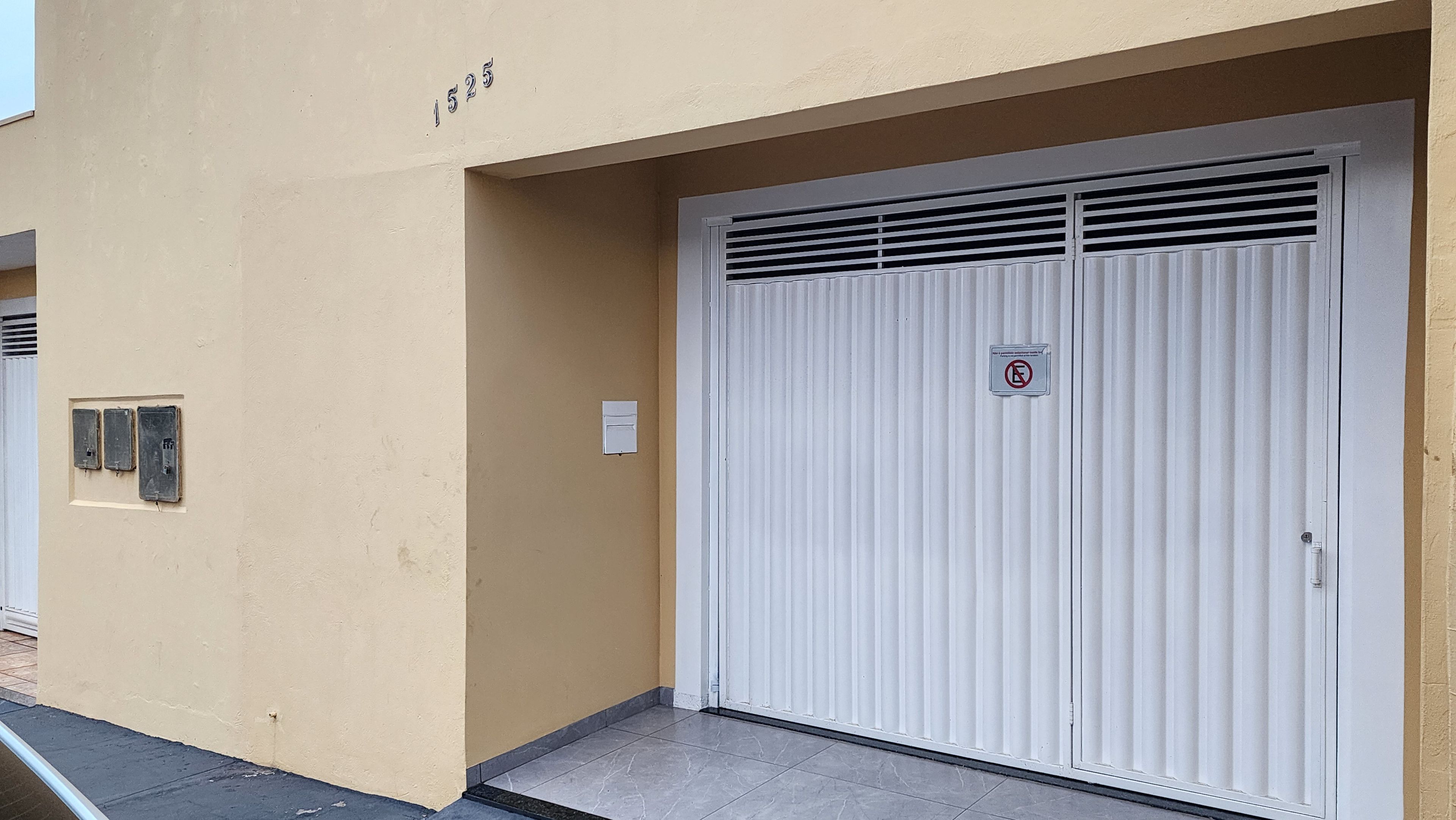 Een gesloten witte garage deur, met een verboden parkeren bord, een meterkast en het nummer '1525' op de muur.