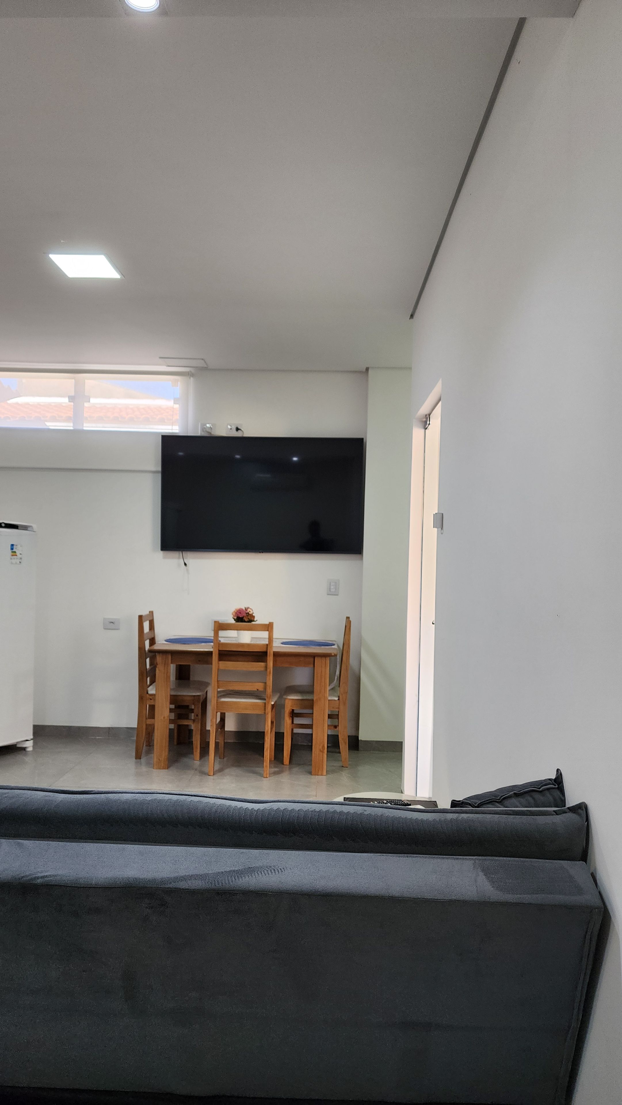 Une pièce comprenant une table à manger, des chaises, un téléviseur à écran plat fixé au mur, un réfrigérateur et un canapé.