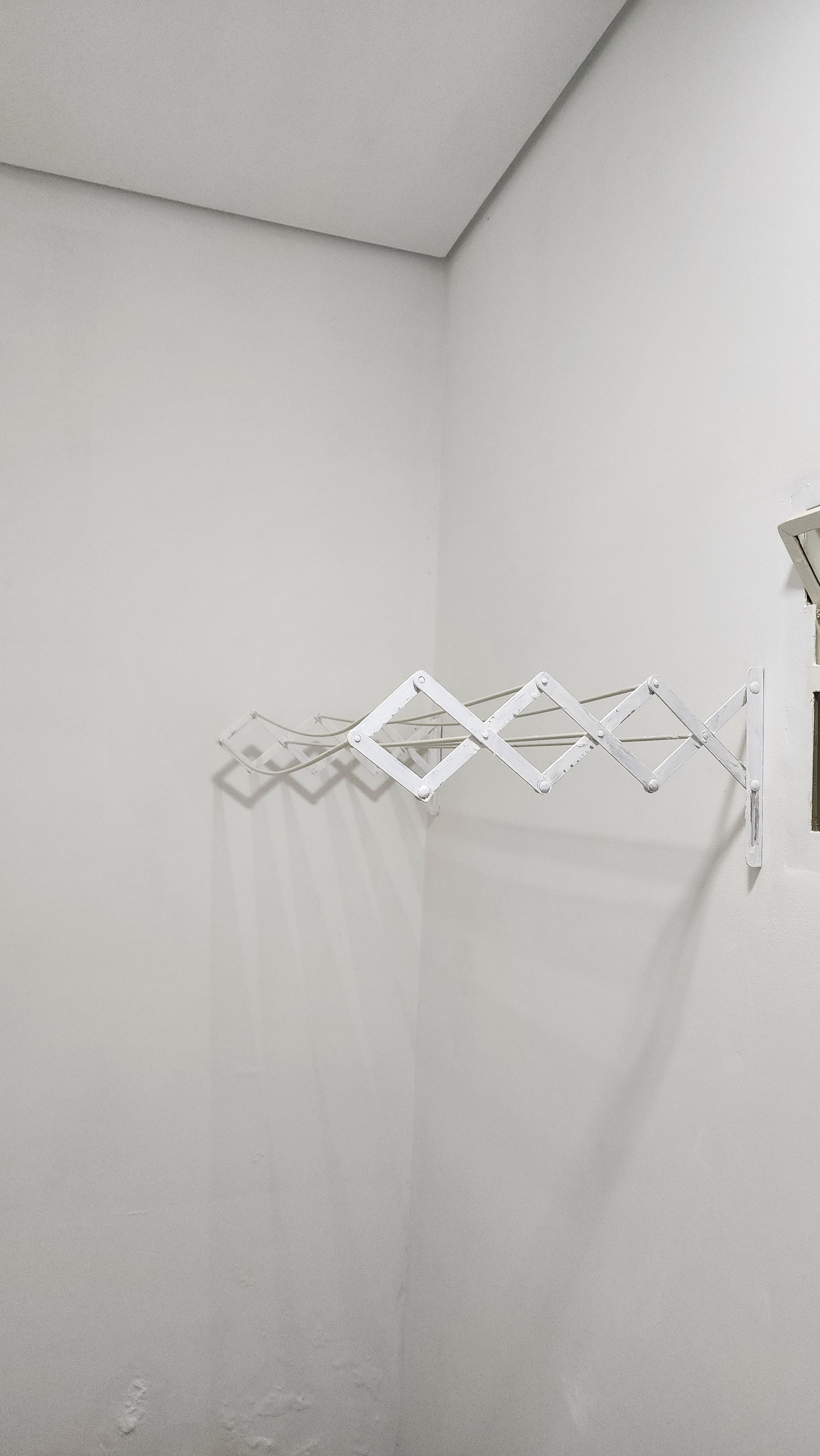 A corner of a room with a white wall and a metal drying rack.