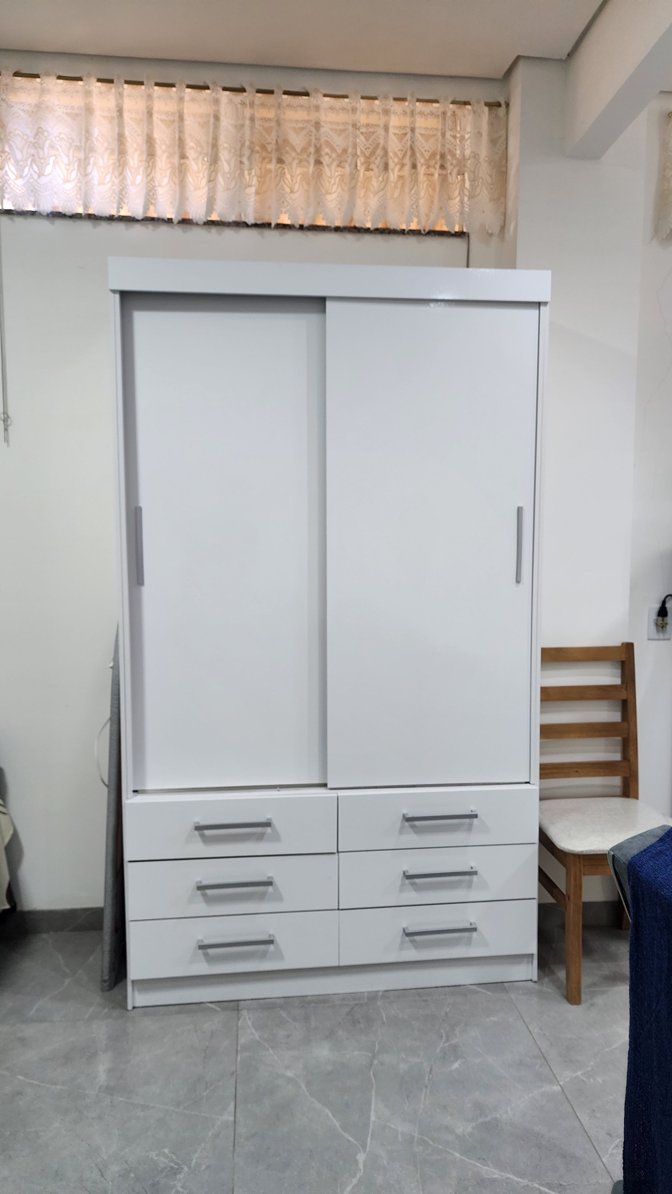 Ein weißer Kleiderschrank mit mehreren Schubladen und ein Holzstuhl.