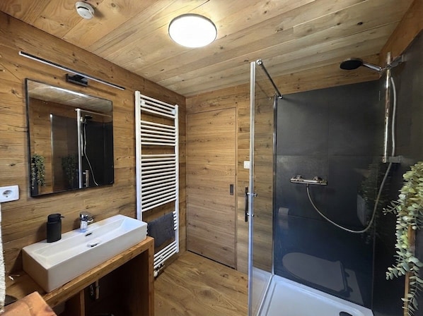 Un bagno con rivestimenti in legno, un lavandino, uno specchio e un box doccia.