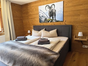 Una stanza con rivestimento in legno, un letto, cuscini, una coperta e una lampada.
