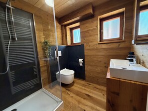 Bagno di una baita in legno con doccia vetrata, un WC e un lavandino.