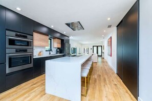 A modern kitchen with built-in ovens, a marble island, and a long countertop. - Casa GaleriaDesign District Art Retreat (Miami)