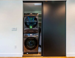 A compact, modern laundry room with a built-in washer and dryer, a control panel, and a small window for natural light. - Casa GaleriaDesign District Art Retreat (Miami)