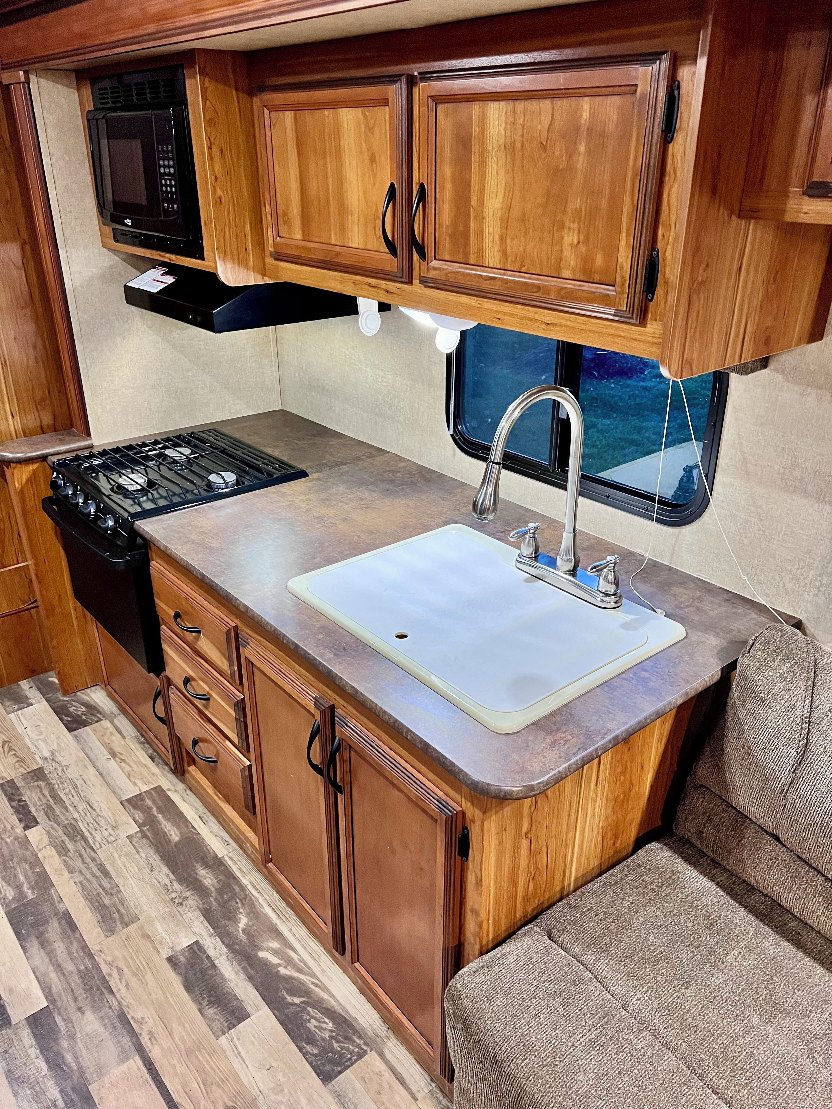 A compact kitchenette with a stove, microwave, sink, and wooden cabinets.