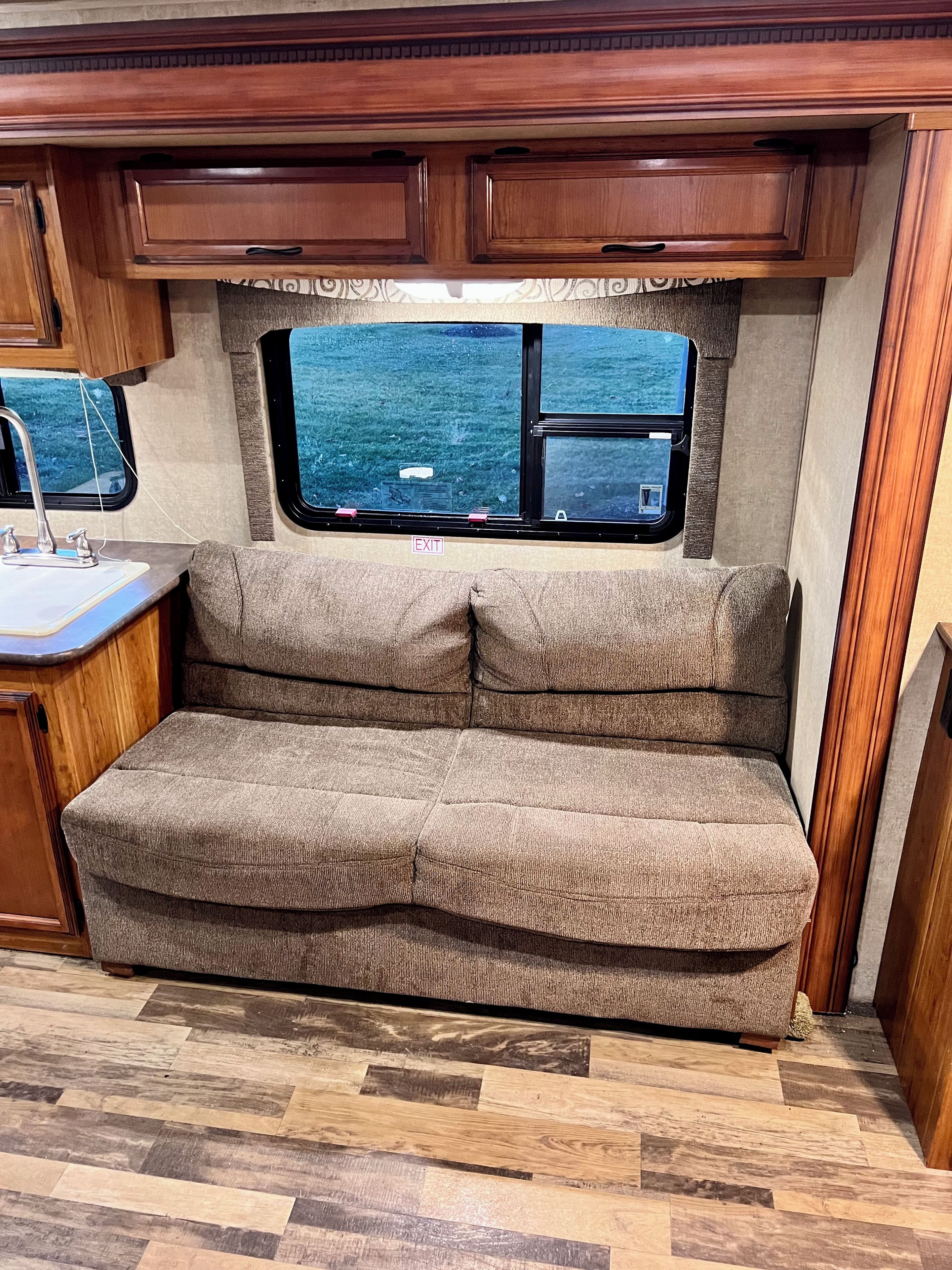 A compact RV interior with a kitchenette, a cushioned seating area, and a window offering a view of the outdoors.