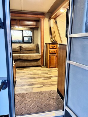 L'intérieur d'un camping-car est aménagé avec un meuble en bois, un coin salon avec des coussins et un tapis à motifs en chevrons.