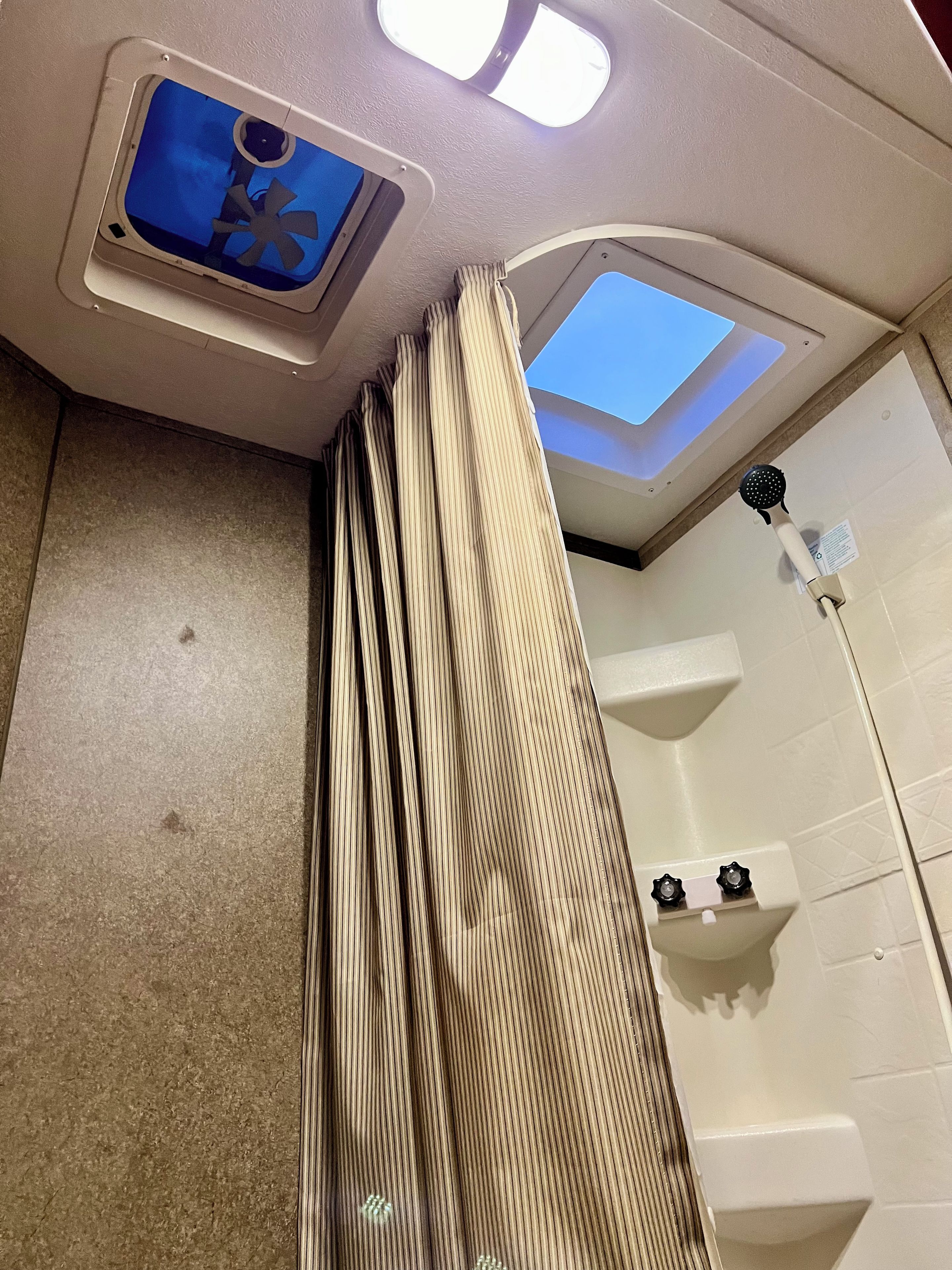 A bathroom with a shower, a ceiling fan, and a skylight.