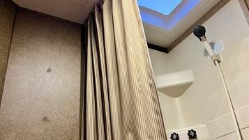 A bathroom with a shower, a ceiling fan, and a skylight.